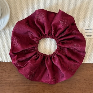 Detailed view of large dark red satin scrunchie with embossed rose floral pattern texture
