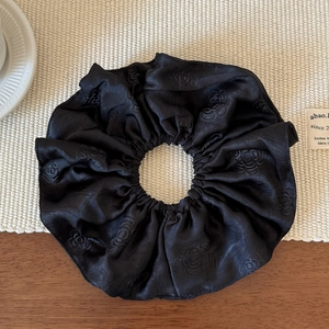 Macro detail of black satin scrunchie with textured floral jacquard and rose patterns