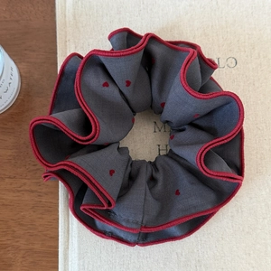 Detailed close-up of dark grey heart-pattern scrunchie with red contrast stitching