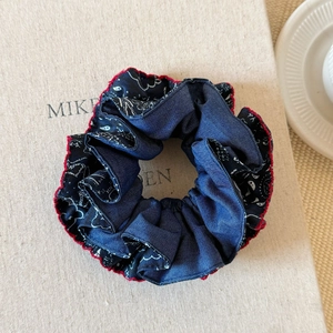 Detailed shot of blue cashew floral scrunchie with red scalloped edges on a textured book
