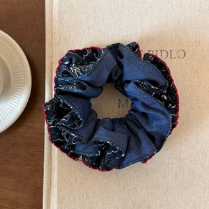 Navy blue paisley scrunchie with red stitching trim on a vintage lifestyle background