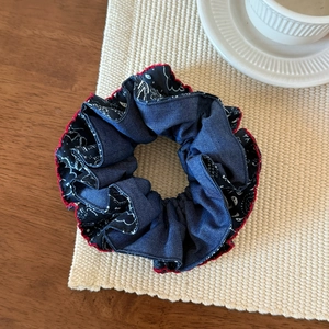 Close-up of navy denim scrunchie with paisley lining and red stitched edges on fabric