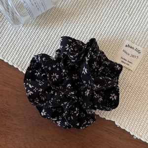 Detailed view of black floral chiffon scrunchie with pink flowers on a textured mat