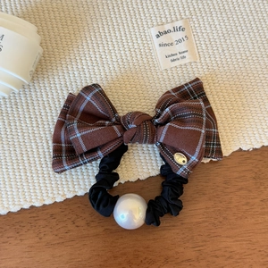 Close-up of brown plaid bow hair tie featuring a gold logo tag and a large white pearl