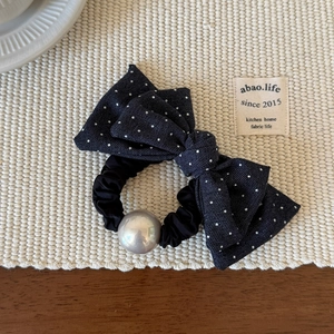Détail d'un chouchou à nœud bleu à pois avec une perle métallique argentée sur tapis