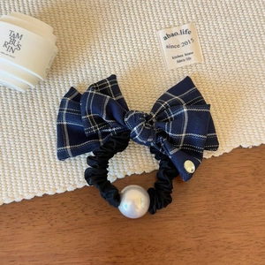 Detail of navy blue plaid bow scrunchie with a large pearl accent and gold metal tag