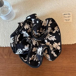 Close-up of black floral chiffon scrunchie with cream flower patterns on a wooden desk