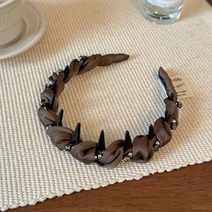 Dettaglio cerchietto in raso plissettato marrone con borchie punk nere e strass argentati