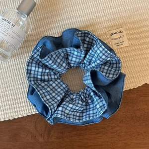 Detailed view of dual-layer blue plaid and denim scrunchie on a woven mat