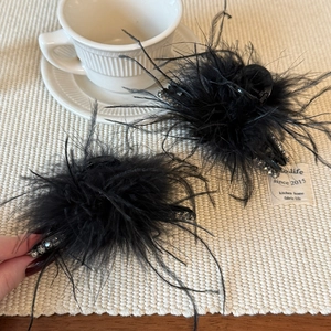 Gros plan de barrettes élégantes en plumes noires et strass sur un fond texturé blanc
