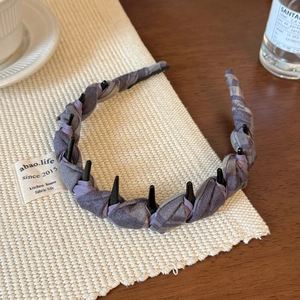 Detail of purple and grey plaid headband with black spikes on a woven mat surface