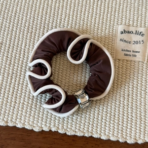 Détail macro d'un chouchou en satin marron avec bords ondulés blancs et cristaux