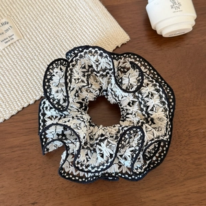Detailed macro view of black and white lace scrunchie with intricate floral embroidery