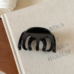 Détail de la grande pince à cheveux noir brillant sur un fond de livre beige minimaliste