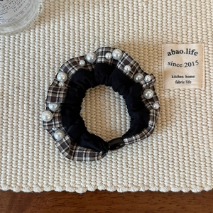 Detailed view of checkered and black fabric hair tie with elegant white pearl accents