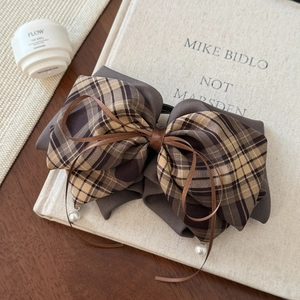 Macro shot of brown plaid bow hair clip with pearl pendants on a textured book