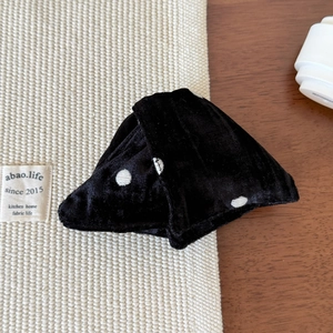 Detailed close-up of a black velvet polka dot hair scrunchie on a woven mat surface