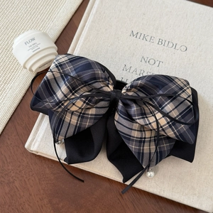 Detail of layered plaid bow hair claw with elegant white pearl accents on navy fabric
