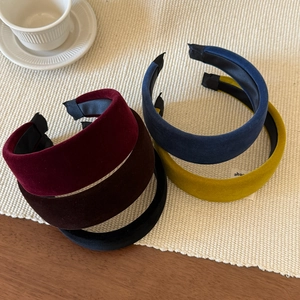 Detailed view of thick velvet headbands in five classic colors on a beige knit surface