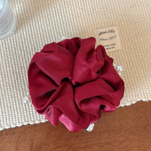 Macro shot of dark red satin scrunchie with elegant pearl accents on a woven mat
