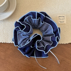 Detail of blue plaid checkered scrunchie with layered fabric on a textured table