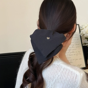 Detail view of a striped fabric bow scrunchie with a metal heart charm on hair