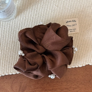 Detail shot of a brown satin scrunchie featuring elegant white pearls and a silky texture