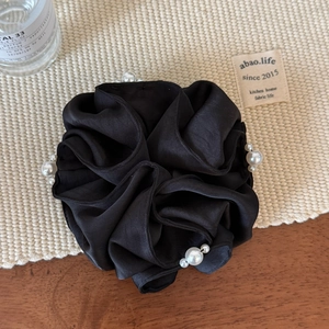 Detailed view of large black satin hair scrunchie with white pearl accents on beige mat