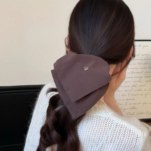 Elegant dark brown striped bow hair tie with silver heart charm worn by a model