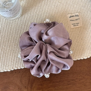 Detail view of a dusty pink satin scrunchie with white pearls on a woven mat surface