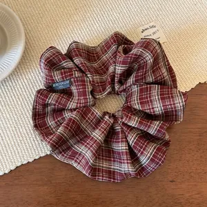 Detail shot of the red plaid fabric scrunchie featuring a decorative brand tag and woven texture