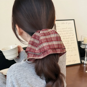 Detail of a large plaid bow hair claw clip styled on a brown wavy ponytail in a cafe
