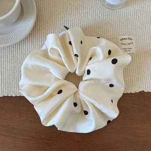 Détail d'un chouchou géant à pois noirs en satin brillant sur un dessous de verre