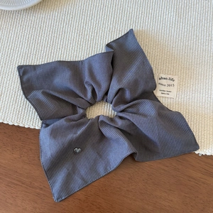 Detail of grey striped fabric scrunchie with silver heart charm and label on wood