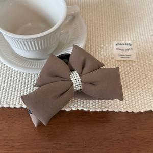 Gros plan d'une pince à cheveux nœud marron avec perles sur un set de table blanc