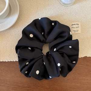 Texture détaillée du chouchou en mousseline noire à pois blancs sur table en bois