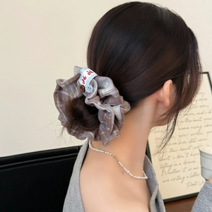 Brown plaid scrunchie with blue ribbon and button detail worn by a model in autumn style