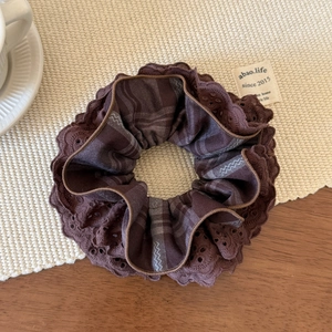 Close-up of brown plaid scrunchie with layered lace edges on a cozy wooden table