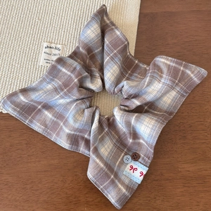 Detailed shot of retro plaid scrunchie with buttons and bow label on a wooden surface