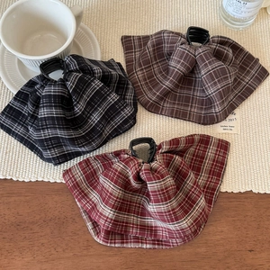 Three elegant plaid bow hair clips in black, brown, and red on a warm tabletop
