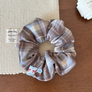 Detail of plaid scrunchie with brown and blue patterns featuring small button accents