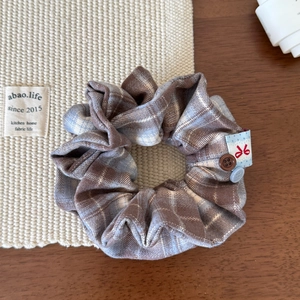 Close-up of a plaid hair scrunchie with detailed fabric texture and decorative buttons