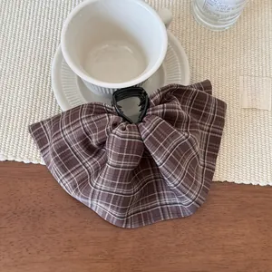 Close-up of brown plaid fabric hair claw clip with bow design on a wooden table