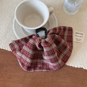 Detail view of large red and beige plaid bow hair claw clip on a cozy wooden table set