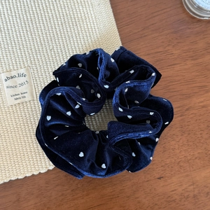 Detailed view of dark blue velvet scrunchie with white polka dots on soft fabric