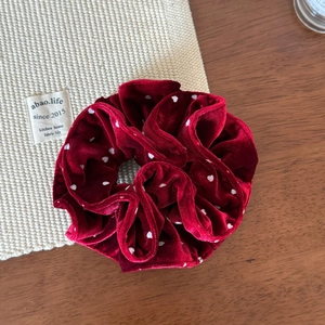 Close-up of a burgundy velvet hair scrunchie with white polka dots on a wooden table