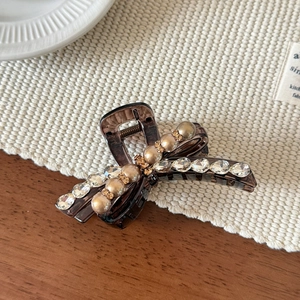 Detalle de pinza para el pelo con lazo marrón, perlas blancas y cristales brillantes
