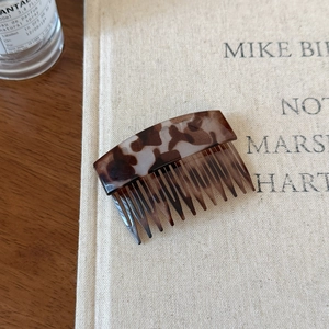 Elegant tortoiseshell acetate hair comb with amber marble pattern on vintage book backdrop