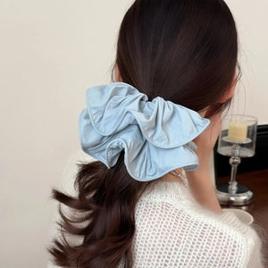 Light blue ruffled fabric scrunchie worn on a low ponytail with layered pleats