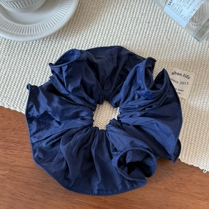 Close-up of elegant deep blue satin scrunchie with soft ruffled folds on a wooden table